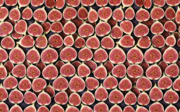Fresh halved figs arranged in a dense repeating pattern background texture, overhead top down view of organic sweet fruit halves for healthy food concepts and culinary designs