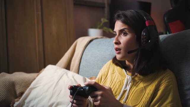 Young Latina woman gaming on her TV at night with a console while talking to friends through her headset, representing online gaming, social connection, technology, and digital entertainment.
