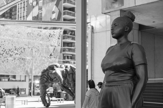 black and white view of "Moments Contained" a 9-foot bronze fictional young Black woman, serenely standing with her hands in her pockets outside the Art Gallery of Ontario, Toronto