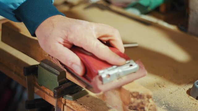 Close-up of a craftsman using a red sanding block to smooth a wooden plank by hand in a workshop. Authentic DIY woodworking footage for craft, carpentry and maker projects