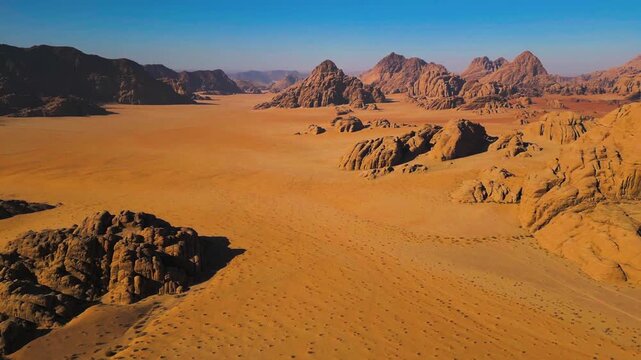 Arid wilderness valleys stretch across vast sandy plains beneath a clear blue sky.