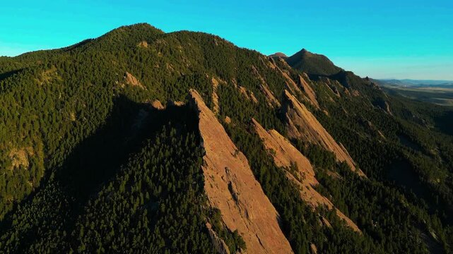 Slanted reddish-brown mountain peaks rise steeply above dense evergreen woodland slopes.