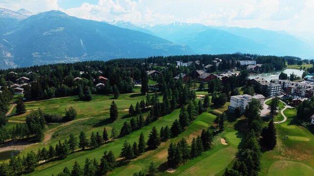 Rows of fir trees line green fairways near Crans Montana, Switzerland, drone panning across them