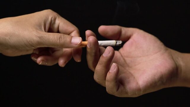 Hand passing a lit cigarette to another person in the dark