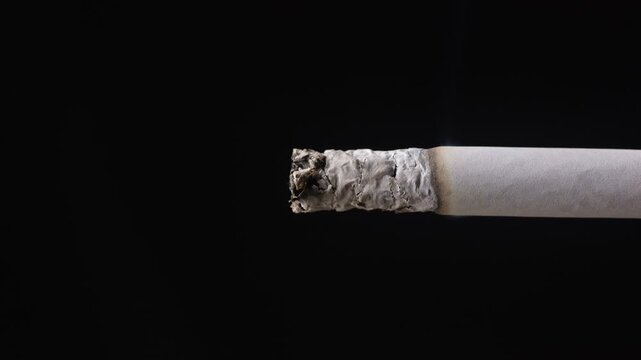 Lit cigarette burning and turning to ash on black background