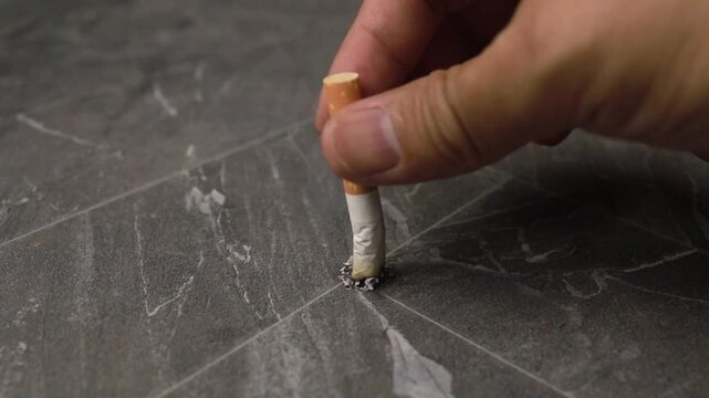 Hand stubbing out a cigarette on a dark tile floor