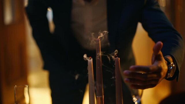 Close up man hand snuffing out candle flame. Smoke rising dinner table evening.