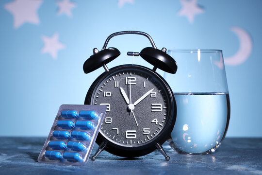 Insomnia and sleep disorder treatment, blue medication capsules with alarm clock and water glass for nighttime health routine and medical therapy