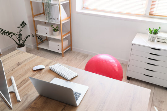 Ergonomic office workspace with exercise ball, remote work wellness and healthy posture in a modern home office with laptop and desk