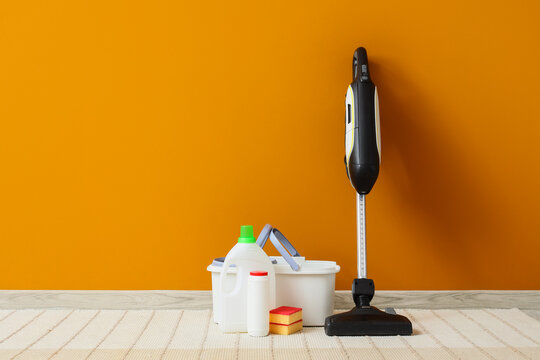 House cleaning and home maintenance, vacuum cleaner with detergent bottles and sponges for spring cleaning chores on a bright orange wall background