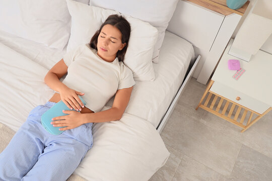 Menstrual pain and period cramps, young woman resting in bed with a hot water bottle and medication for relief of abdominal discomfort and illness