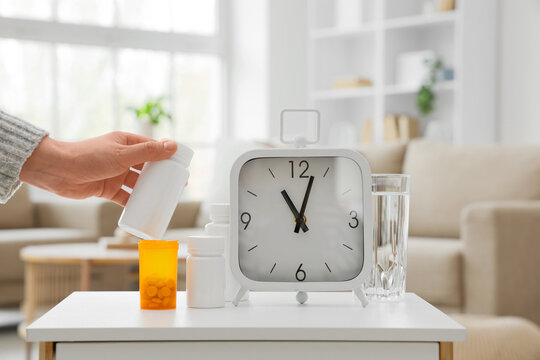 Medication adherence and healthcare routine, person taking daily pills with alarm clock and water glass on bedside table for health management and wellness