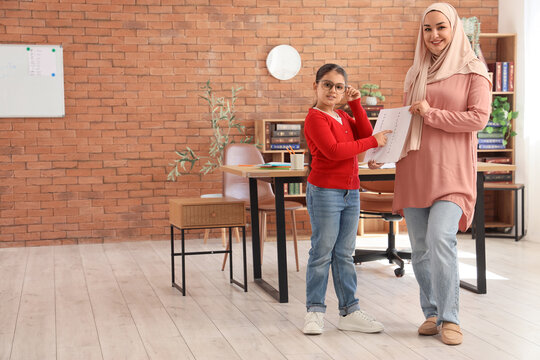 Education and homeschooling, Muslim mother and daughter studying together with schoolwork in a home office environment with a brick wall background