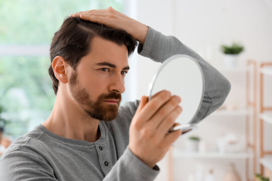 Hair loss and male grooming, man checking hairline in mirror for signs of thinning hair or balding in a home bathroom setting