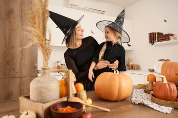 Obraz premium Halloween family fun, mother and daughter wearing witch hats preparing pumpkins for holiday celebration in a modern kitchen home interior