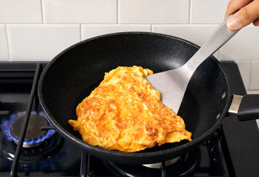 Cooking golden omelette in black frying pan on gas stove