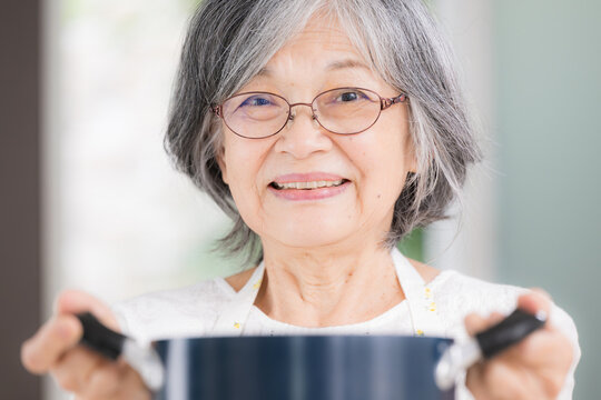 An energetic elderly Japanese woman cooking at home; cooking for herself, housework, healthy eating, healthy life expectancy, independent senior living; close-up of her smiling face looking 