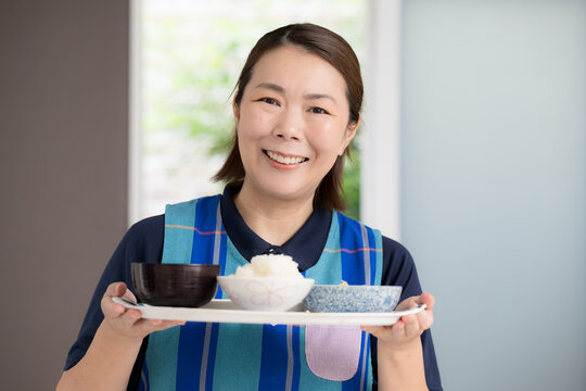 食事を配膳する笑顔の介護スタッフ、訪問介護、家事代行で食事を提供のホームヘルパーイメージカメラ目線
