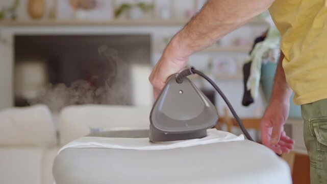 Close up view of a man ironing laundry on an ironing board at home, with steam coming from the hot appliance. Domestic chores and household activities for wrinkle-free and tidy clothing