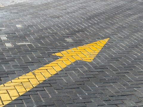 High angle view of yellow painted arrow on grey herringbone interlocking paving blocks, urban directional sign texture background use
