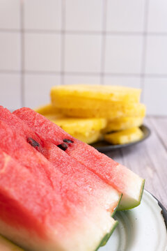 Close-up of watermelon and pineapple slices on plates against a tiled wall