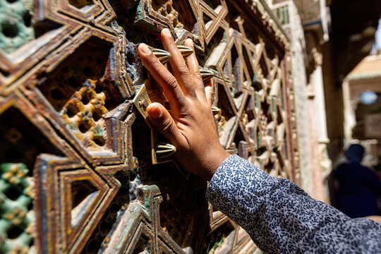 close-up view of a person's hand touching an intricately carved wooden screen, which is a classic piece of Islamic architectural latticework in Fes old town Morocco
