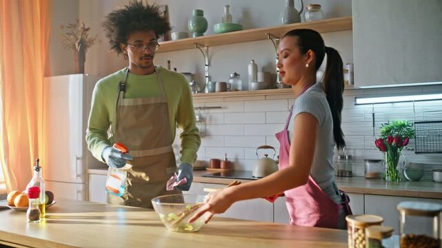 Boyfriend cleaning kitchen counter. Girlfriend hugging partner apron cooking.