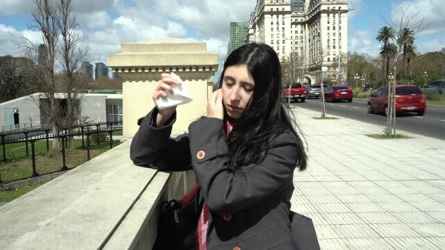 Young latina woman with hay fever sneezing into a tissue in the city