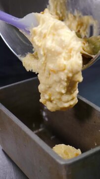 Close-up of hand in glove lifting thick lumpy cream mixture from metal bowl with purple spatula. Professional pastry kitchen, baking preparation process. Slow motion vertical Full HD shot