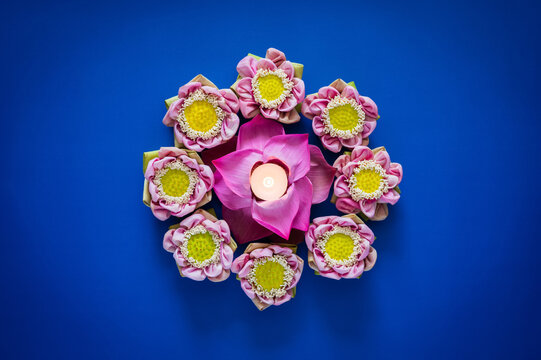 Loy Krathong festival flat lay with a glowing candle and pink lotus flowers on a blue background.