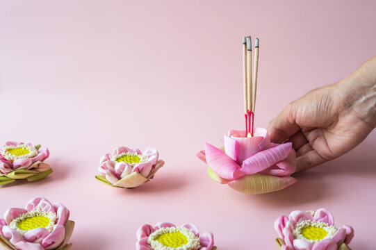 Hand holding Loy Krathong krathong with candle and incense on pink background.
