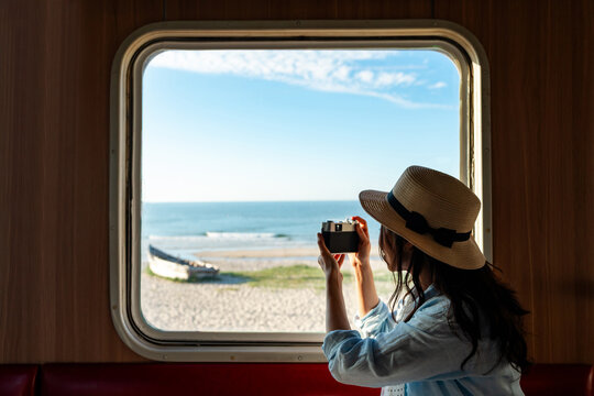 Solo female traveler taking pictures of sea view while traveling by train on summer vacation
