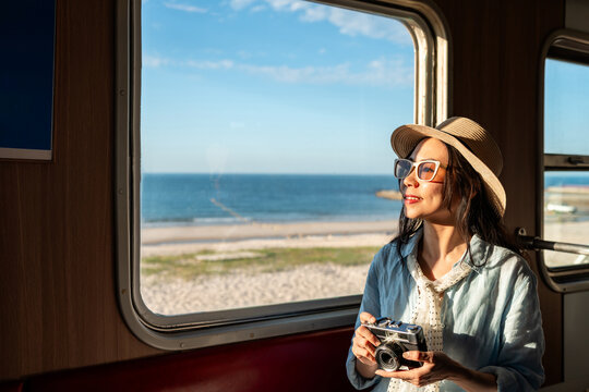 Young female traveler holding a retro camera and enjoying the sea view while traveling by train during her vacation