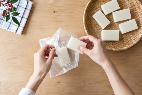 Hands packing rectangular Japanese kiri mochi into a clear storage bag for practical New Year food preparation