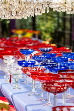 Dining table with tablecloth filled with colorful crystal vintage glasses for luxury event reception, preparations for celebrations, grand outdoor settings, banquet table with glassware for drinks.