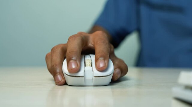 Hand using a computer mouse on office desk, Close-up of a person using a computer mouse on a desk, with a blurred blue shirt and soft office background.