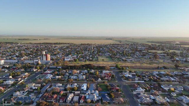 Aerial drone view of Horsham, Victoria, Australia, with houses, residential streets, grain silos, regional railway, and vast, flat agricultural fields stretching toward the distant horizon
