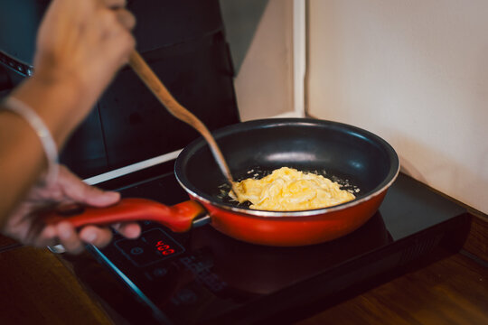 Close up of woman cooking scrambled eggs in a red non stick frying pan.