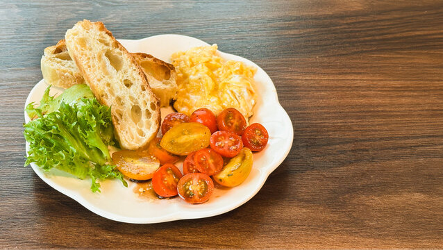Healthy breakfast with scrambled eggs, toasted, sliced cherry tomato, and fresh greens on wooden surface.