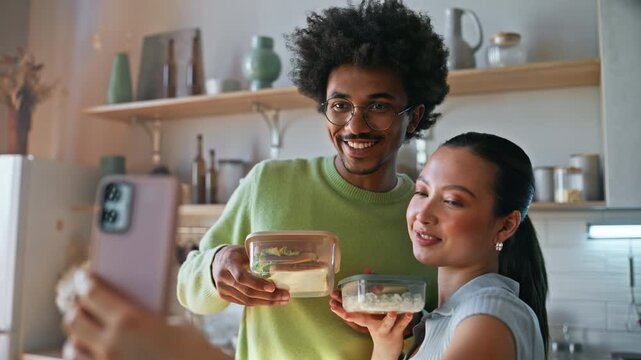 Interracial couple taking selfie meal prep container. Girlfriend kissing man.