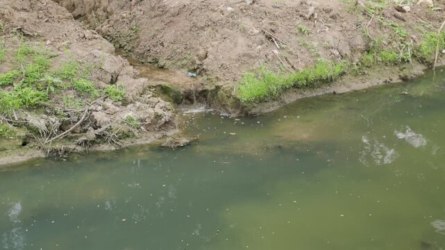 Polluted shallow river with sediment and wastewater discharge, symbolizing human impact, environmental destruction, ecosystem degradation, water contamination.