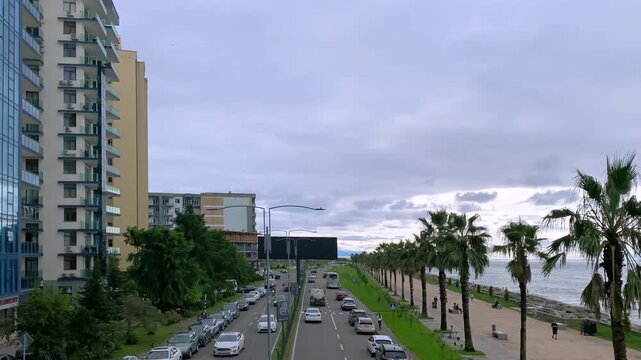 Traffic moving along Batumi boulevard, elevated view of residential towers beside the Black Sea, suitable for real estate, urban planning, coastal development