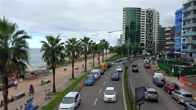 Traffic moving along Batumi coastal avenue, elevated view, with high-rise apartments and Black Sea frontage for real estate, urban development, investment