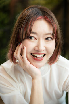Portrait of a smiling woman resting her chin on her hand outdoors.