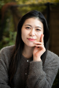 Close-up portrait of a woman with dark hair resting her hand on her cheek.