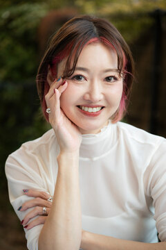 Portrait of a woman with arms crossed, smiling gently outdoors.