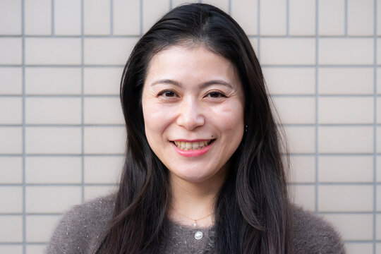 Close-up portrait of a smiling woman against a modern tile wall.