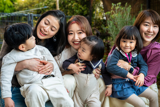 Group portrait of smiling mothers and their children sitting together outdoors.