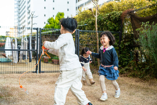 Children playing and running outdoors with a jump rope in a sunny yard.