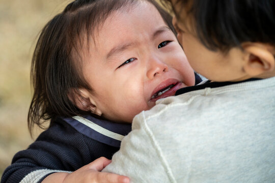 Close-up of a crying toddler being comforted and held in arms.